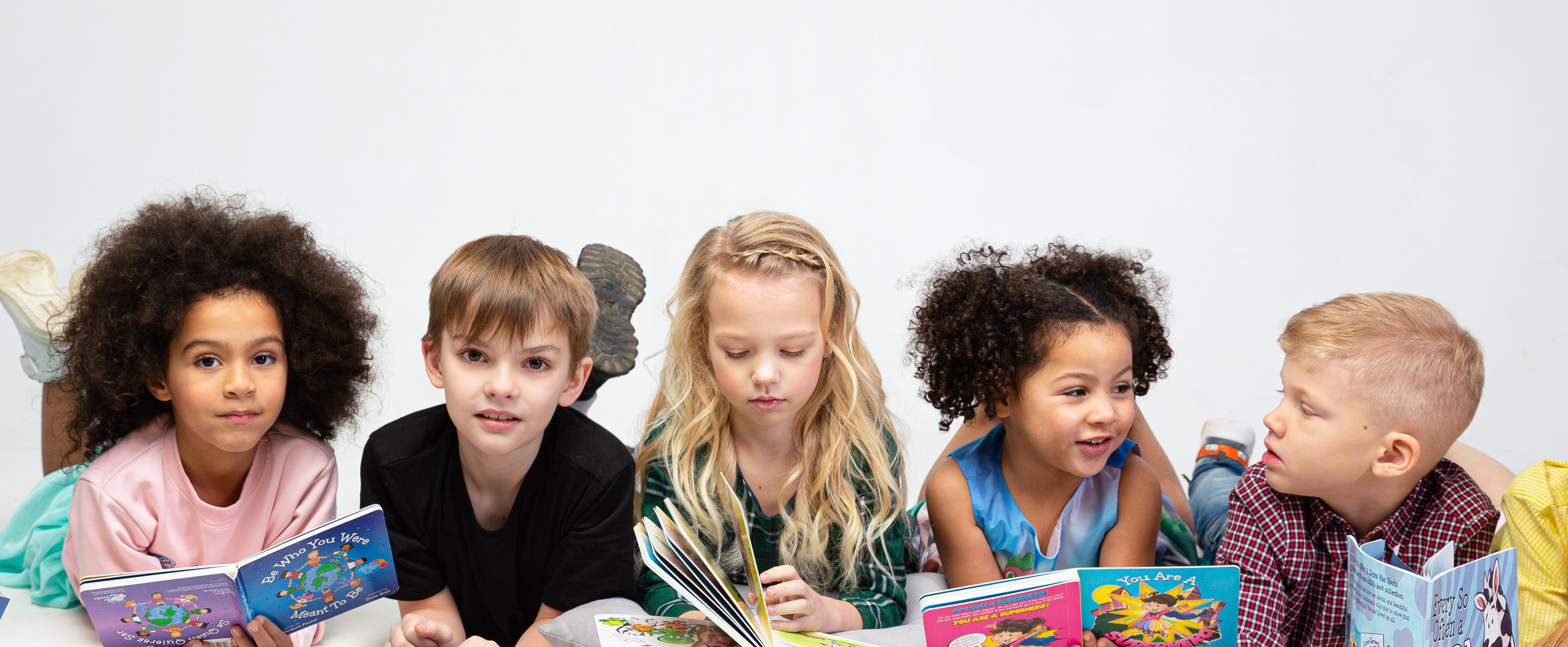 Children reading books from The Be Books series by Lauren Grabois Fischer, including titles like 'Be Who You Were Meant to Be,' 'The Light Within Me,' and 'Every So Often a Zebra Has Spots,' promoting themes of kindness, confidence, and mindfulness.