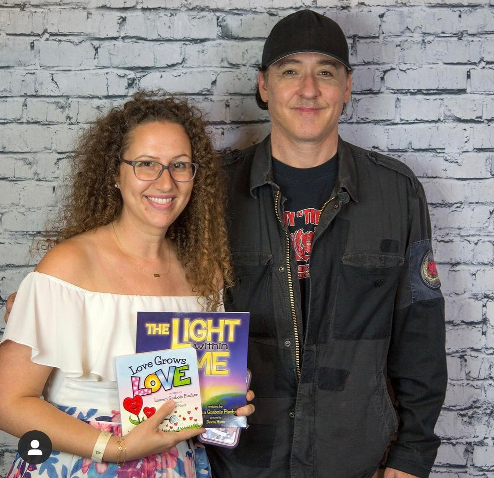 Lauren Grabois Fischer with actor John Cusak holding  'The Light Within Me' and 'Love Grows Love' while at a book event